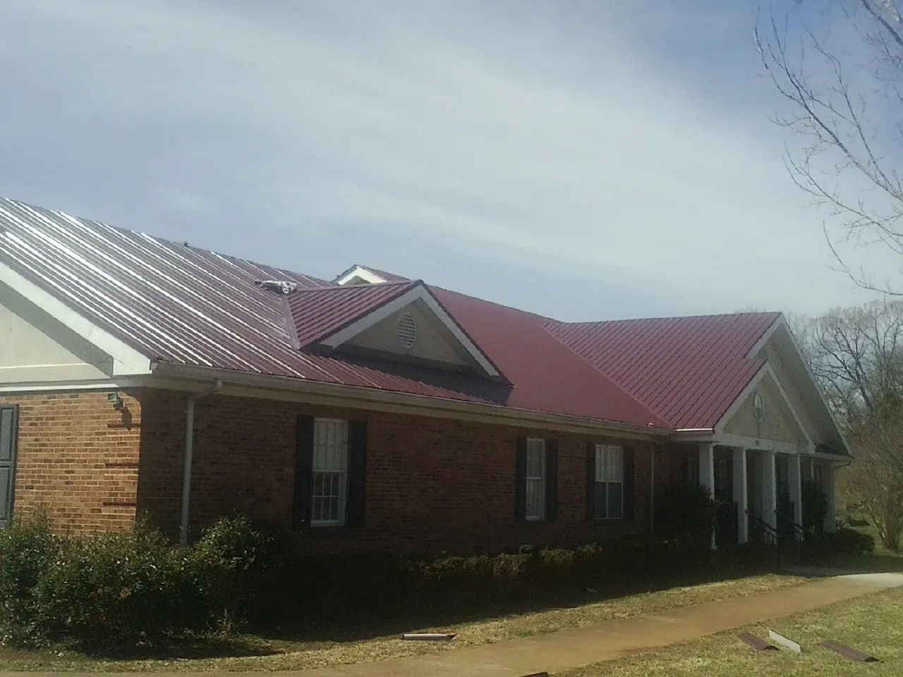 Red metal roof with gabled entries on a long brick building, from a Hail Damage Roof Repair job in Portland