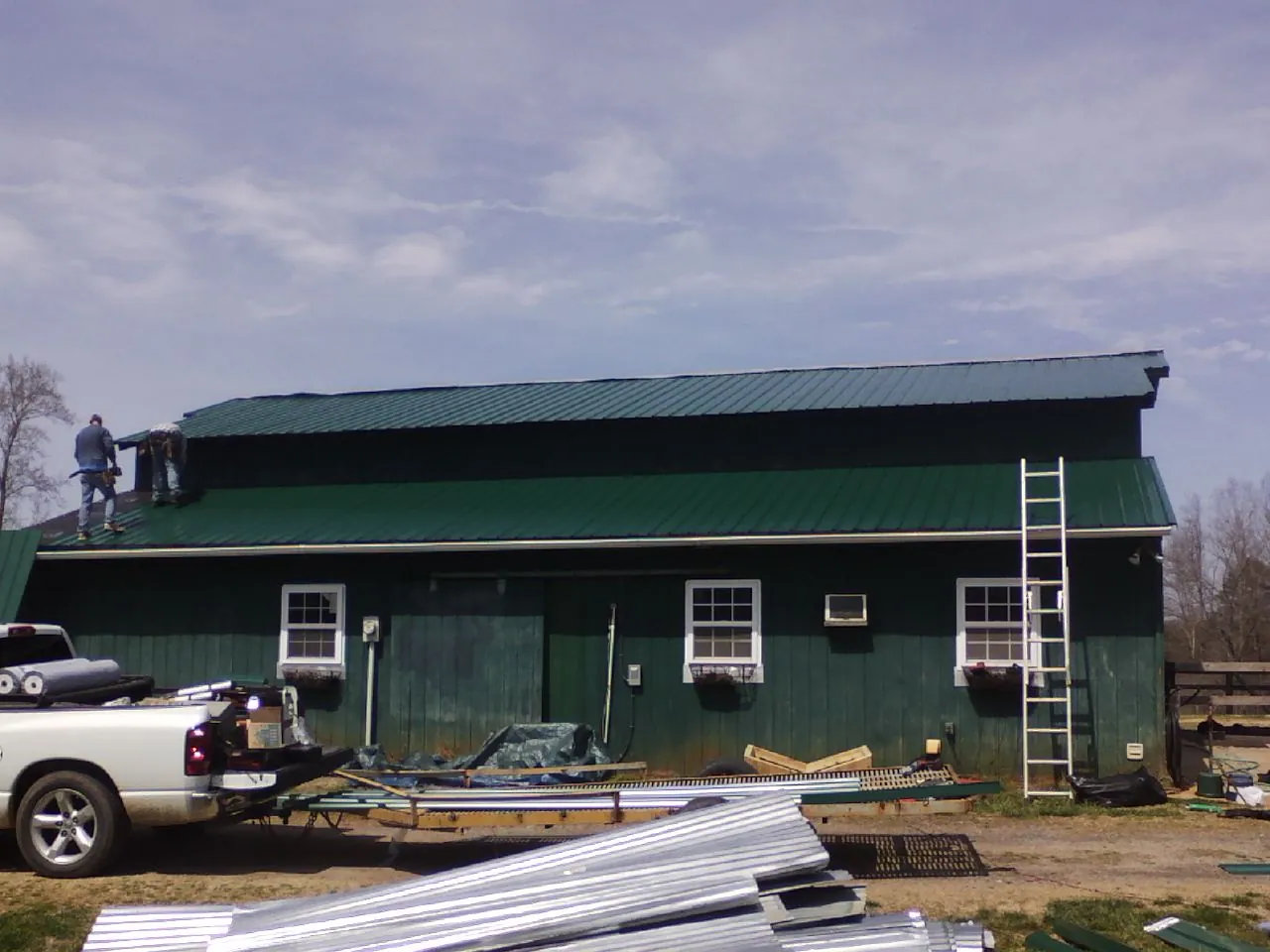Crew installing green metal roofing on a large green barn in Portland